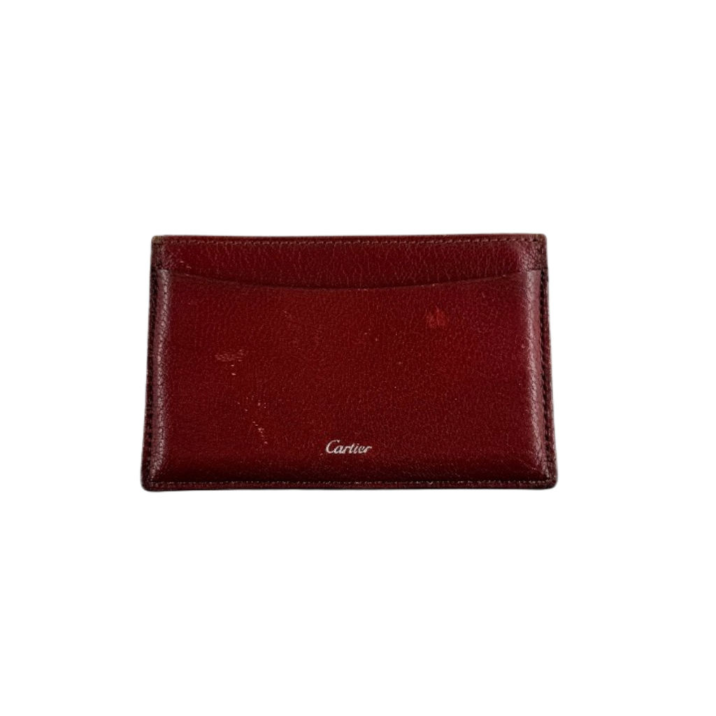 Must de Cartier burgundy leather cardholder with visible natural texture and Cartier script logo, photographed against a clean background.