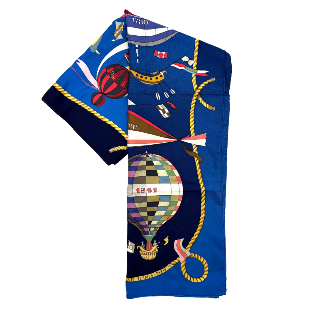 Hermès Les Folies du Ciel silk scarf in vivid multicolours with whimsical hot air balloons and golden rope border on a blue background.