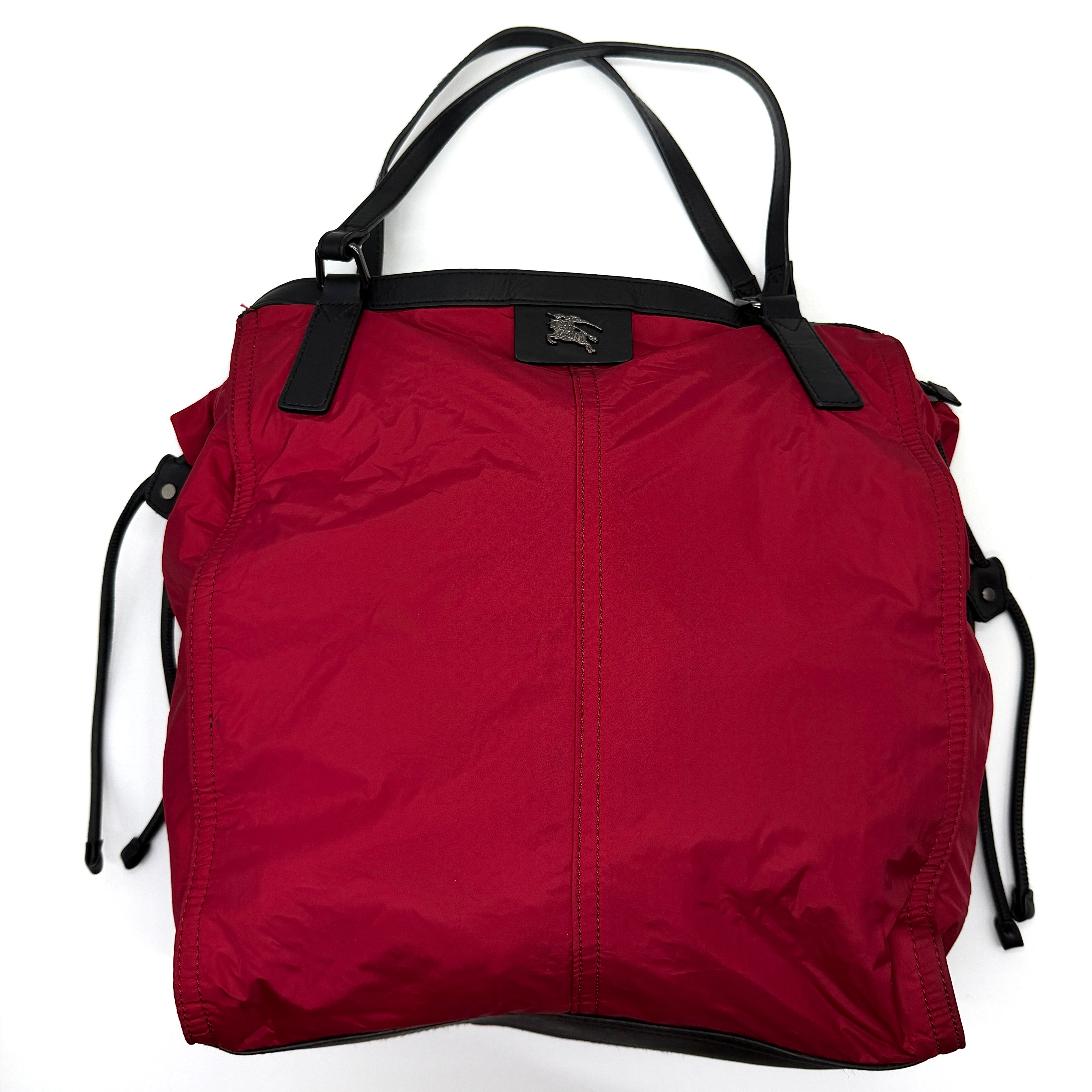 Burberry Buckleigh Nylon Tote Bag in red with black leather trim, drawstring sides, and signature Burberry check interior.