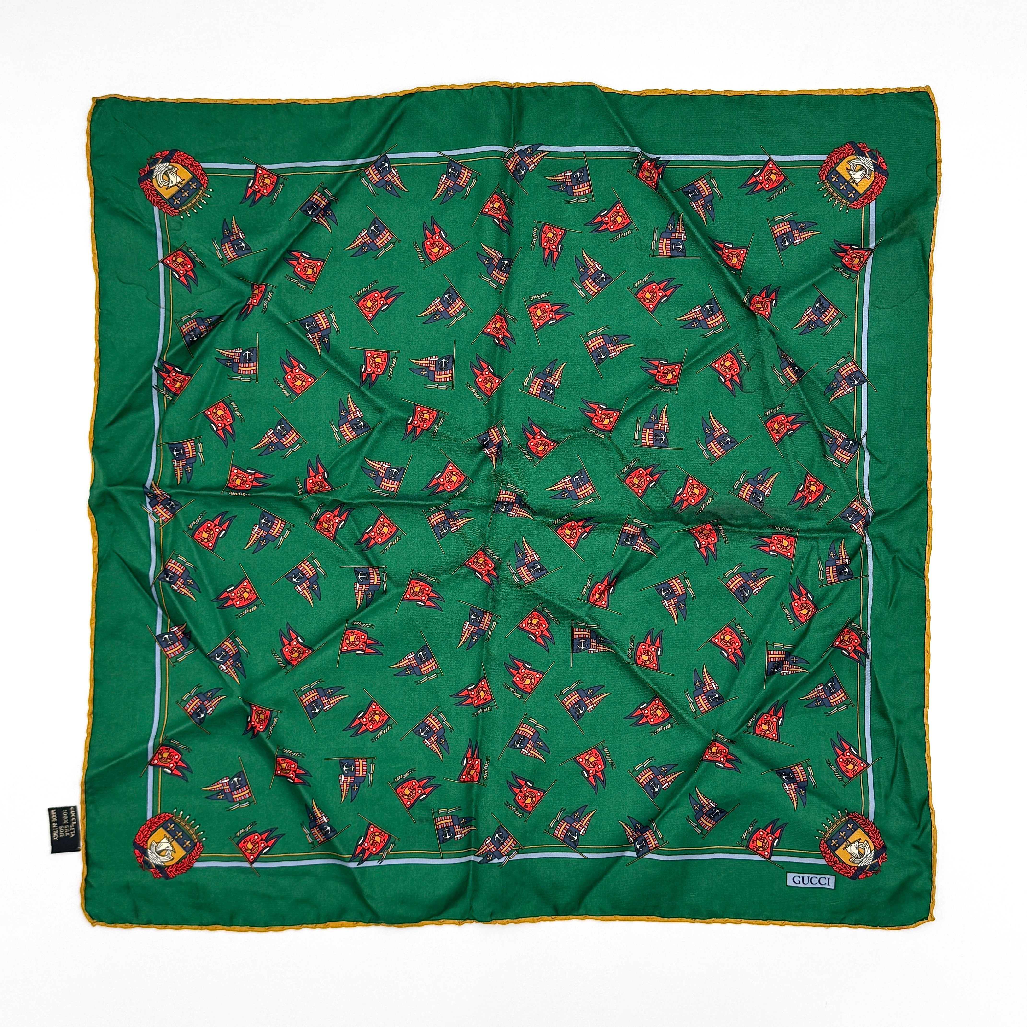 Gucci green silk pocket square with intricate pattern, featuring a central emblem and contrasting yellow edging.