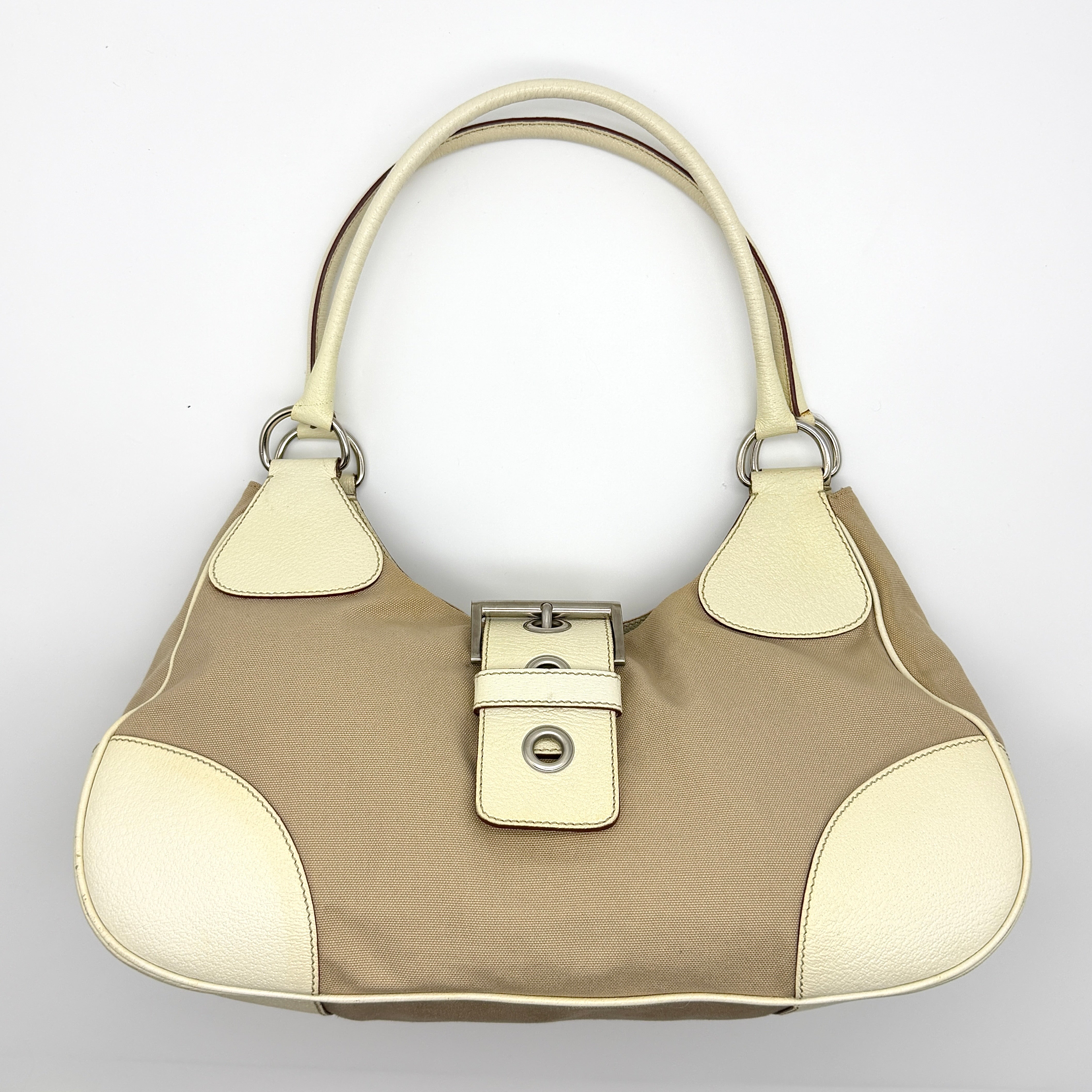Prada Enamelled Moon Shoulder Bag in beige and cream canvas with leather trim, silver-tone hardware, and sculptural buckle detail.
